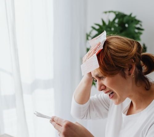 Woman sitting at a table stressed about bills in a bright living room