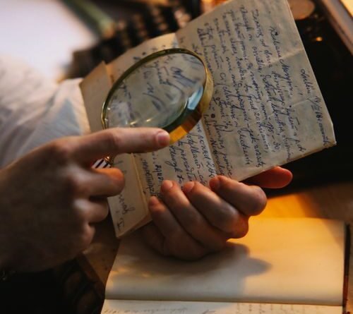 Close-up of hands examining a document with a magnifying glass