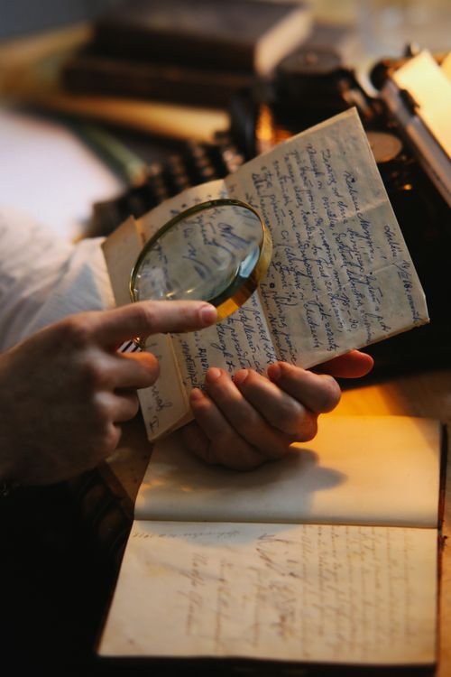 Close-up of hands examining a document with a magnifying glass