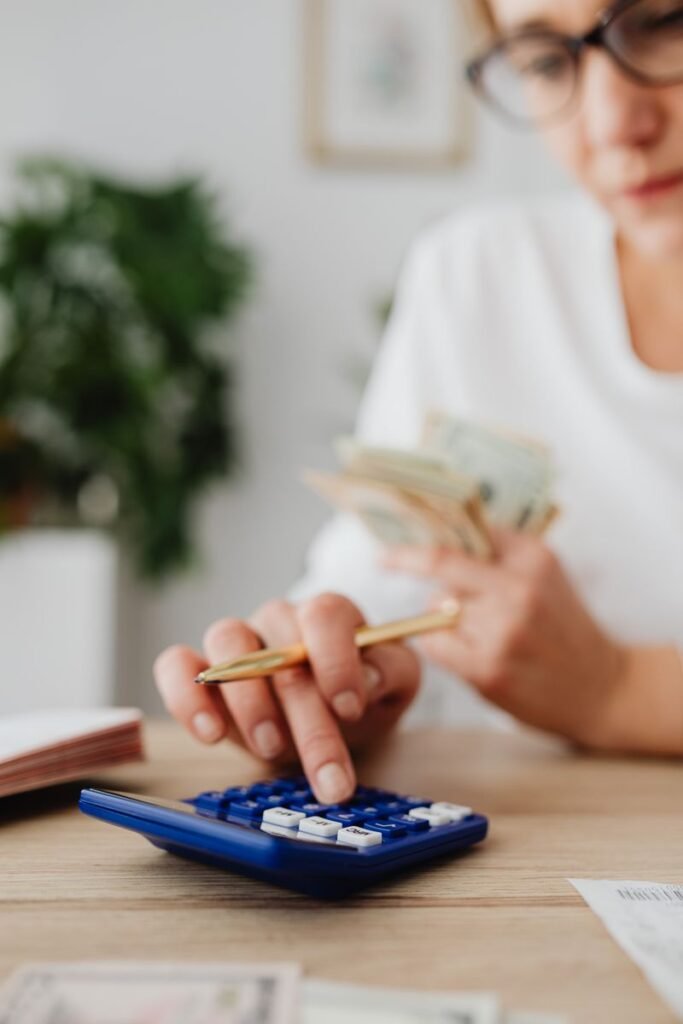 A woman using a calculator while holding cash, reviewing household bills at a desk