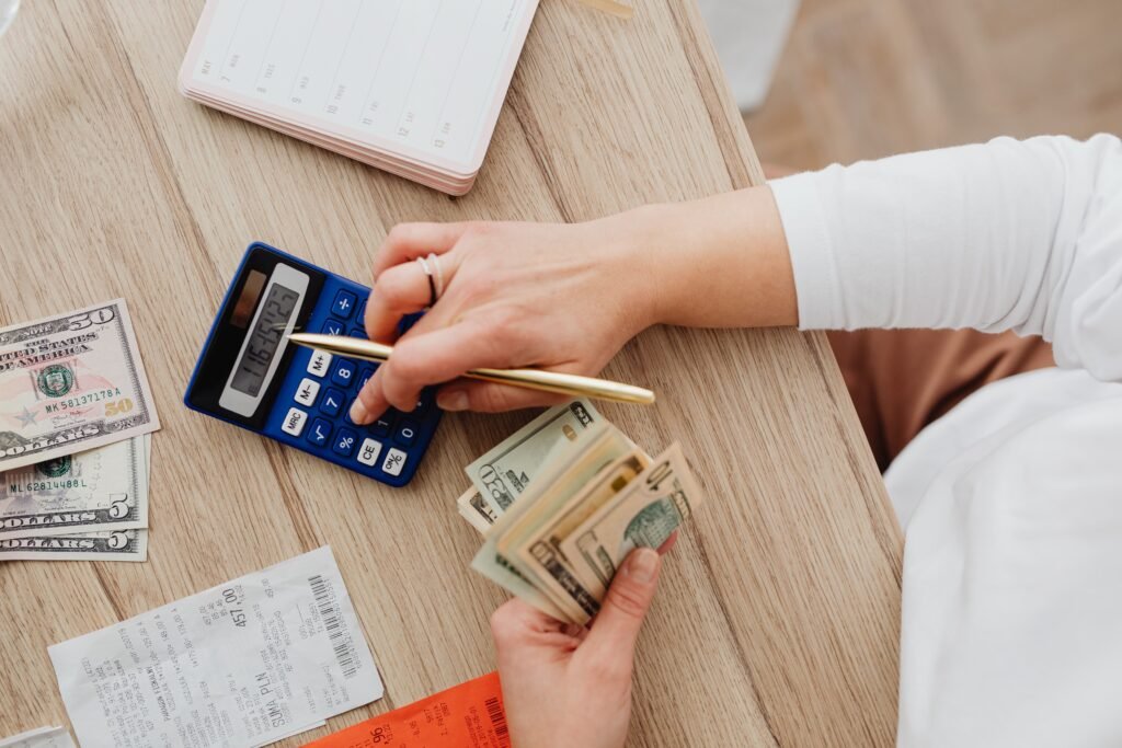 Person using a blue calculator while holding dollar bills, illustrating debt settlement fee calculations