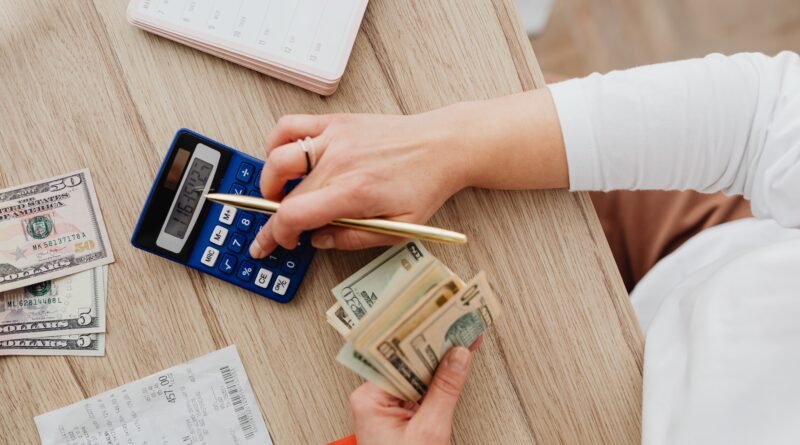 Person using a blue calculator while holding dollar bills, illustrating debt settlement fee calculations