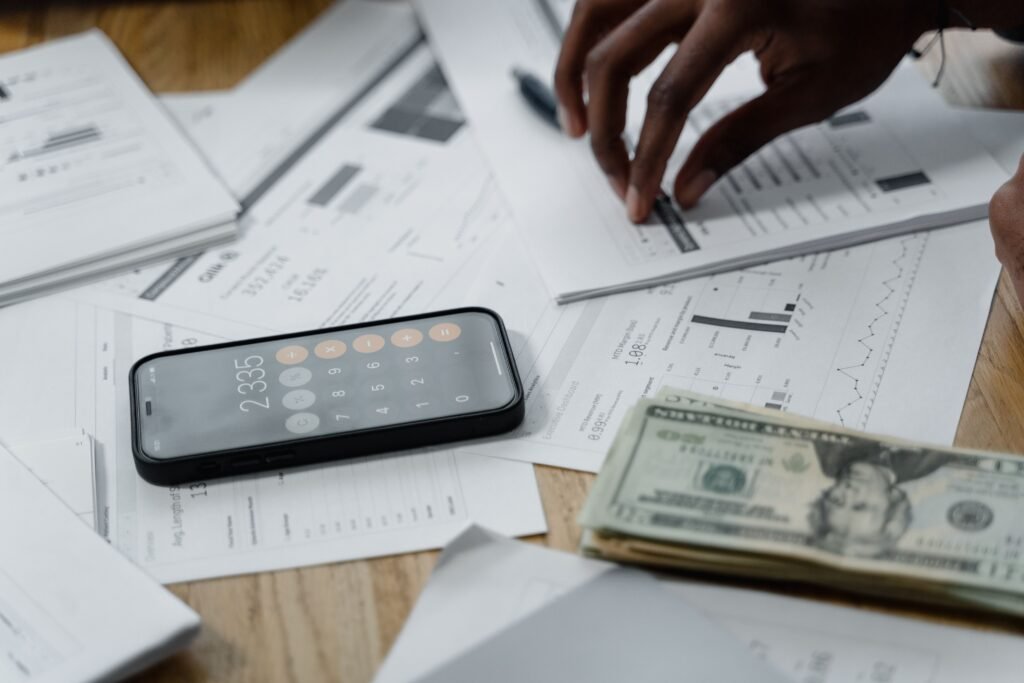 Close-up of hands calculating financial data with a smartphone, cash, and reports on a table