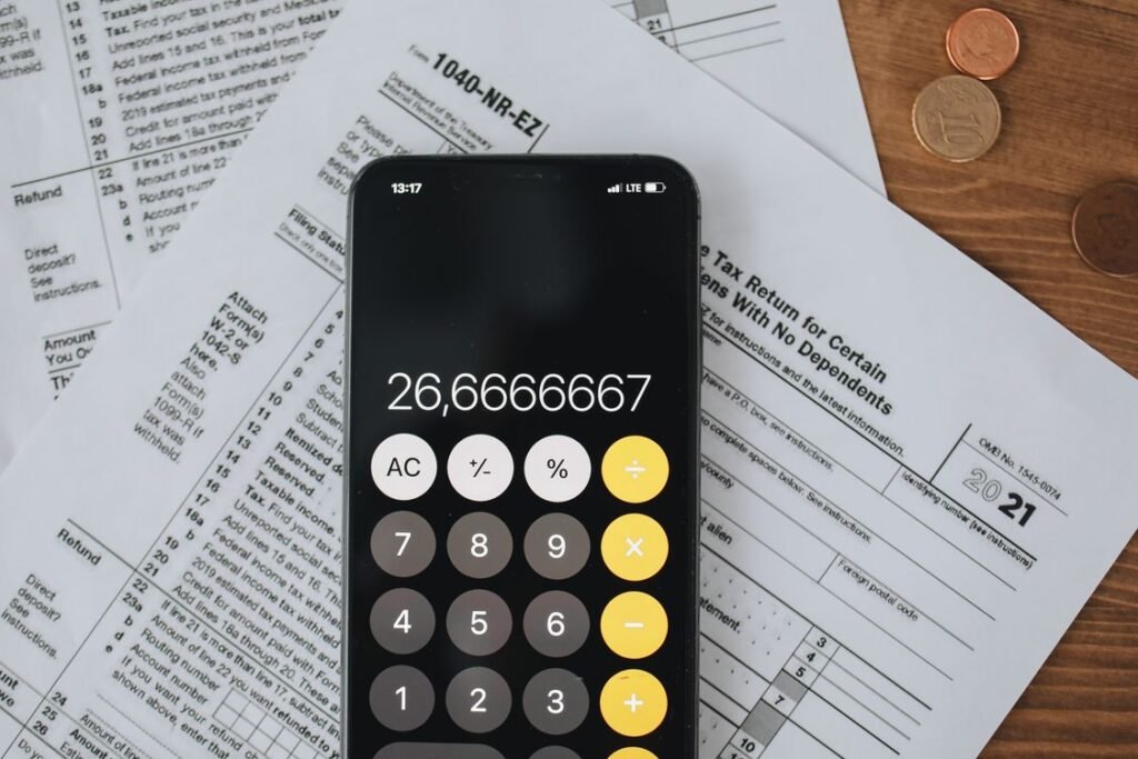 Smartphone calculator over tax forms with coins on a wooden desk