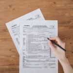 Person filling out IRS tax forms and paperwork on a wooden desk