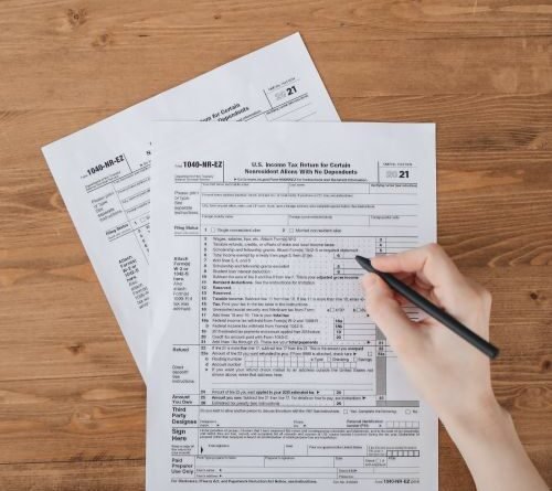 Person filling out IRS tax forms and paperwork on a wooden desk