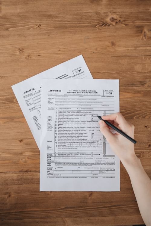Person filling out IRS tax forms and paperwork on a wooden desk