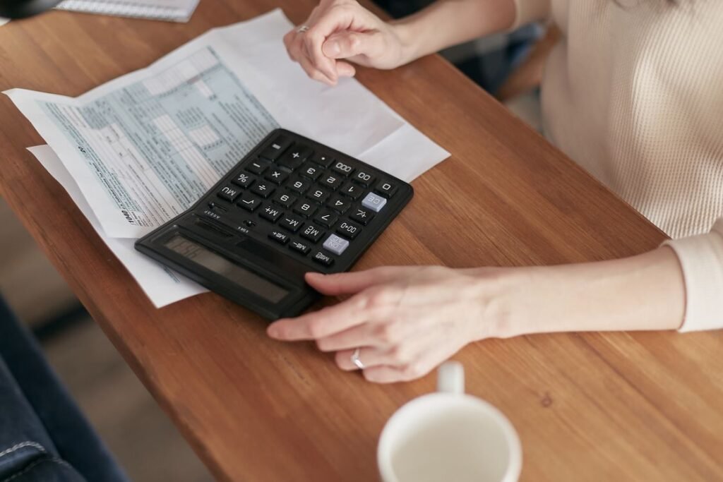 Person using a calculator to plan finances and budget at a wooden desk