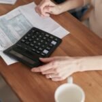 Person using a calculator to plan finances and budget at a wooden desk
