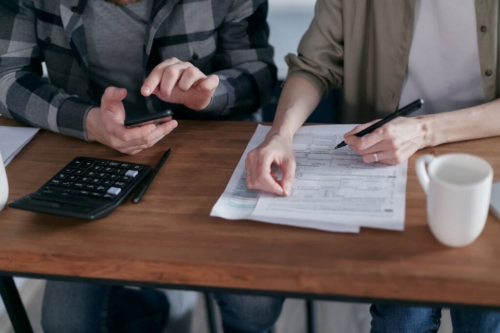 Two people working together on tax forms using a calculator at a wooden desk