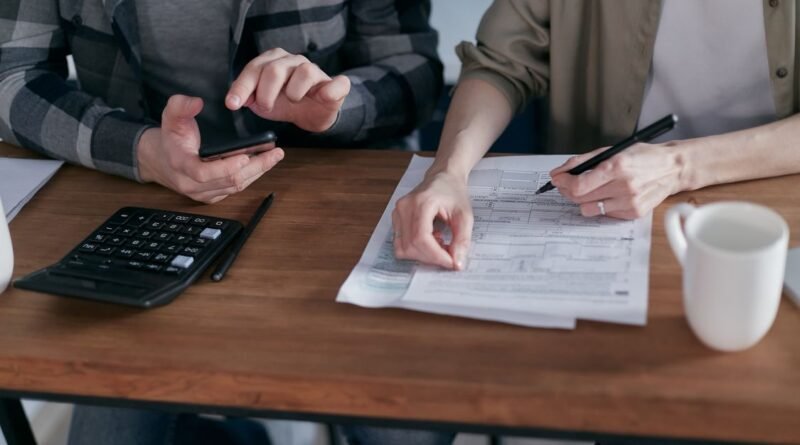 Two people working together on tax forms using a calculator at a wooden desk