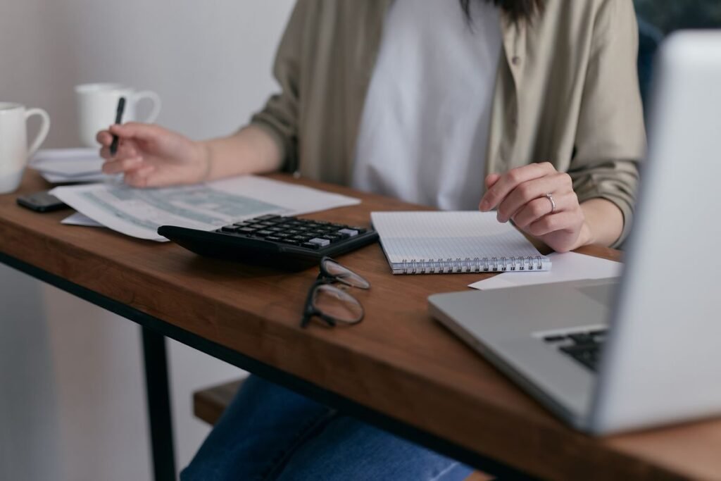 Person using a calculator with credit card bills and a laptop on a home desk