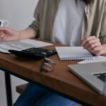Person using a calculator with credit card bills and a laptop on a home desk