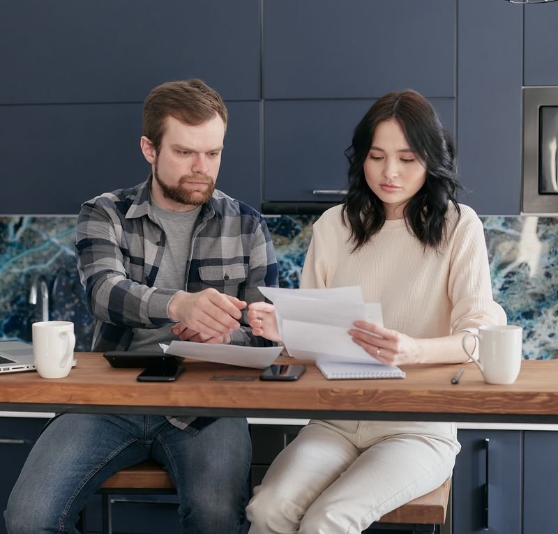 A young couple reviews bills and budget together in a modern kitchen
