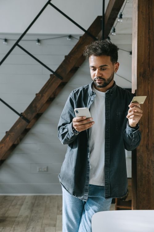Man holding a cellphone and credit card, checking the impact of debt settlement on his credit score