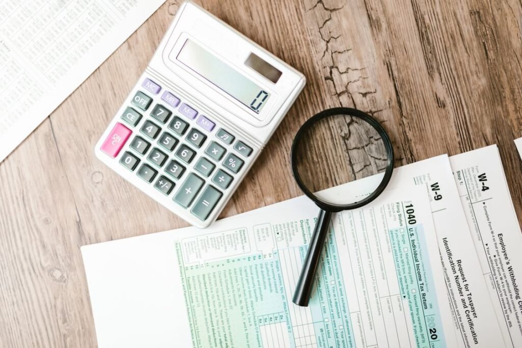 Tax forms, calculator, and magnifying glass arranged on a wooden desk for loan application review