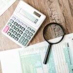 Tax forms, calculator, and magnifying glass arranged on a wooden desk for loan application review