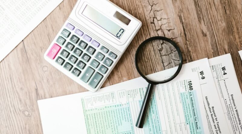 Tax forms, calculator, and magnifying glass arranged on a wooden desk for loan application review