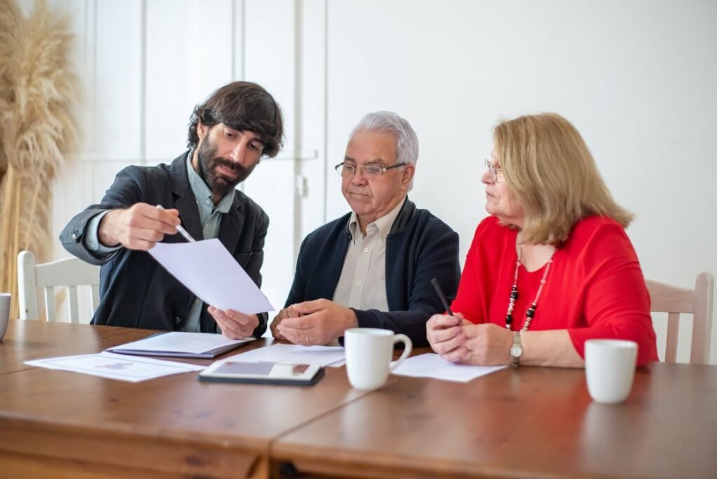 Elderly couple discussing documents with advisor at a wooden table indoors